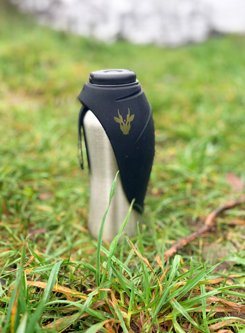 Black and silver bottle with a Muntjac logo on grass