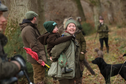Brand Ambassador Emma and our mini brand ambassador Harry in a forest setting with a dog, wearing outdoor clothing.